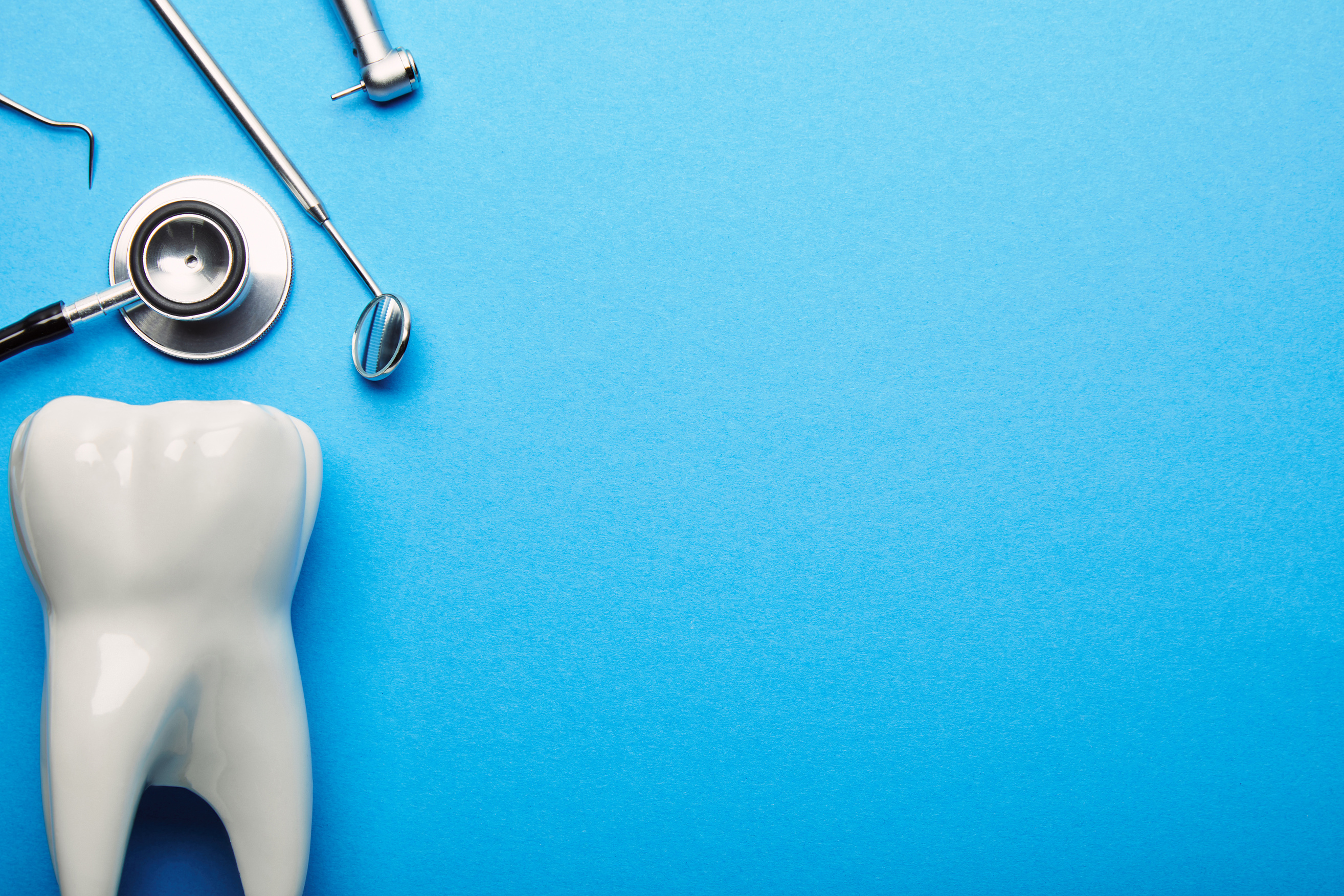 flat lay with tooth model, stethoscope and sterile dental instruments arranged on blue backdrop